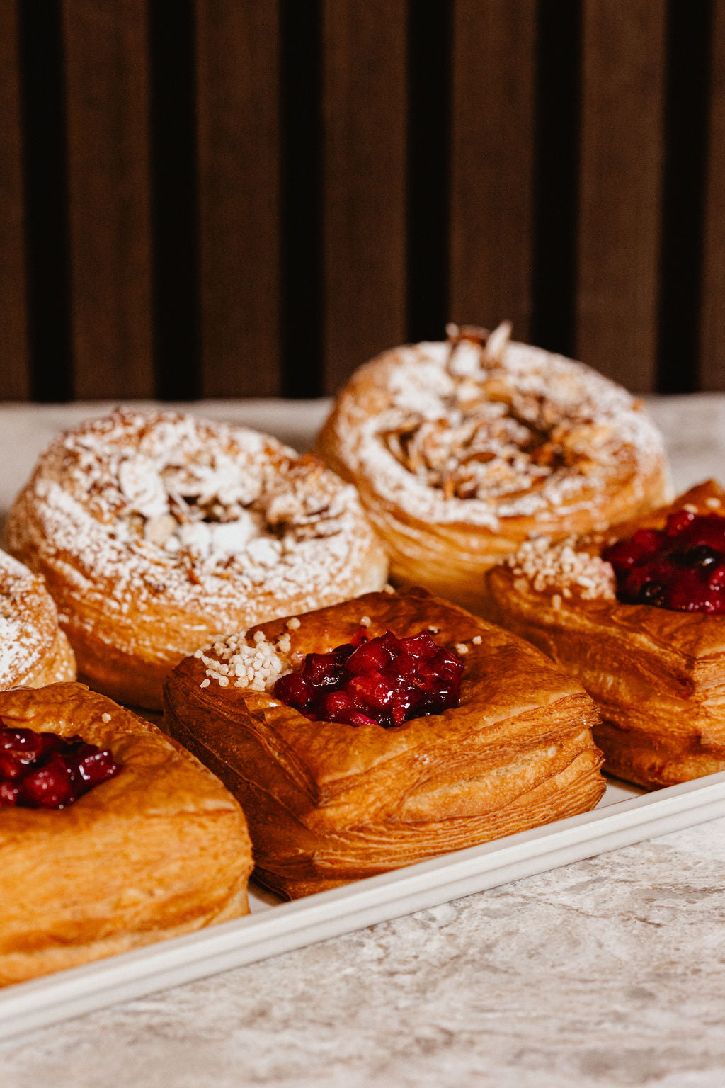 A close-up of freshly baked pastries at Black Sheep Coffee, featuring flaky golden layers dusted with powdered sugar and topped with vibrant fruit fillings. The assortment includes almond danishes and fruit danishes, showcasing the shop's dedication to artisan baking. Perfect for coffee pairings, breakfast, or a sweet treat during the day. Keywords: Black Sheep Coffee pastries, fresh baked goods, artisan almond danishes, fruit danishes, local coffee shop treats.
